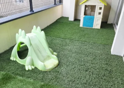 Photo de l'extérieur de la micro crèche de Juvisy-sur-Orge avec une pelouse synthétique, une petite maison et un petit toboggan pour enfants